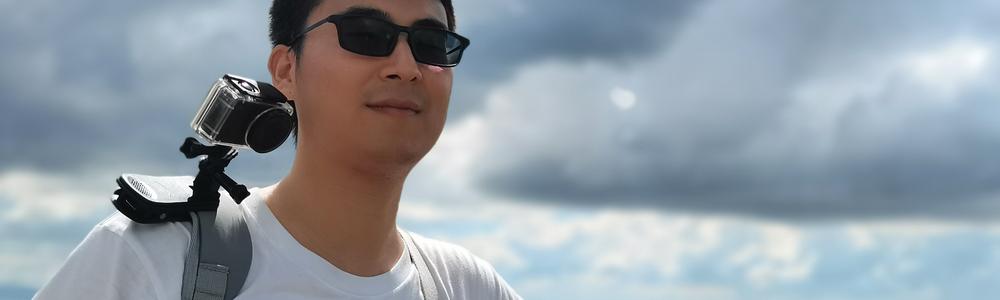 A man with sunglasses standing outside, clouds and sky above