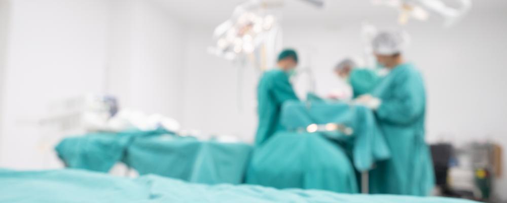 Operation pågår i operationsrum i bakgrunden av den här bilden.