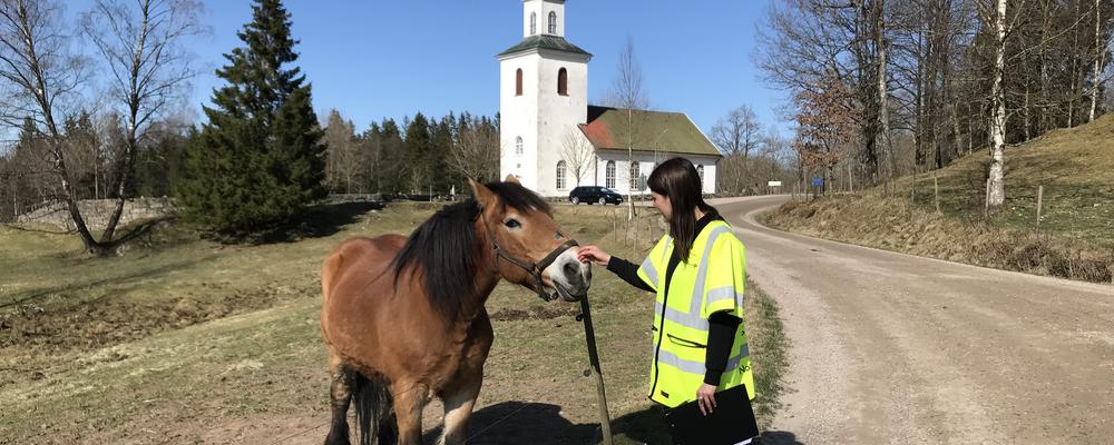 Alumn Stina Ekberg står bredvid en häst, framför en kyrka, foto.