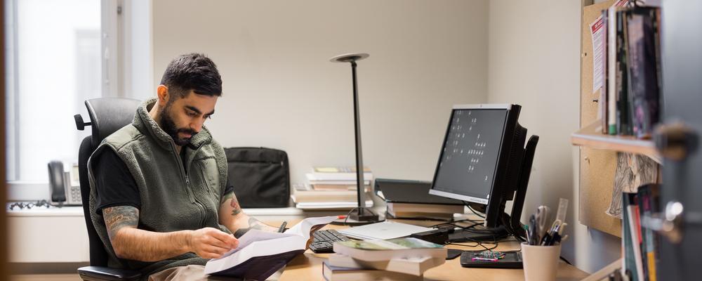 en manlig forskare sitter vid sitt skrivbord och läser