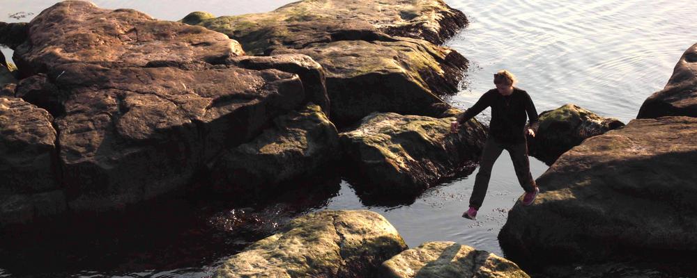 Tjej med svarta kläder och rosa gympaskor går på klippor vid havet