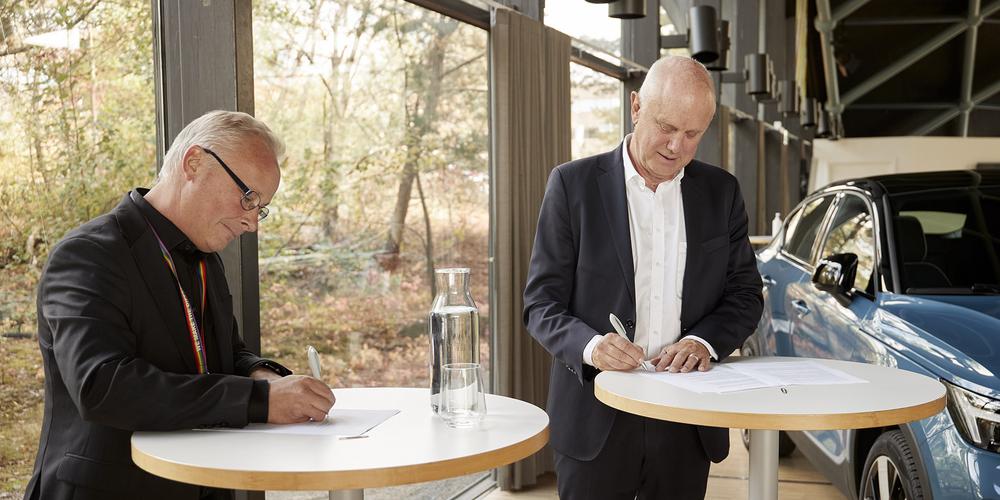 Kristian Abel and Per Cramér stand at their respective tables and sign the agreement