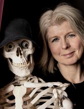 Anna Luther med kikar fram bakom draperiet med skelettet Åke.