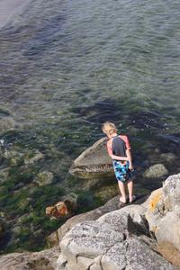 Poke som står på klippor och tittar ner i havet
