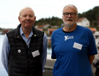 Två män i 70-årsåldern står framför havet bärandes tröja med trycket "Kivik tång" samt namnskyltar