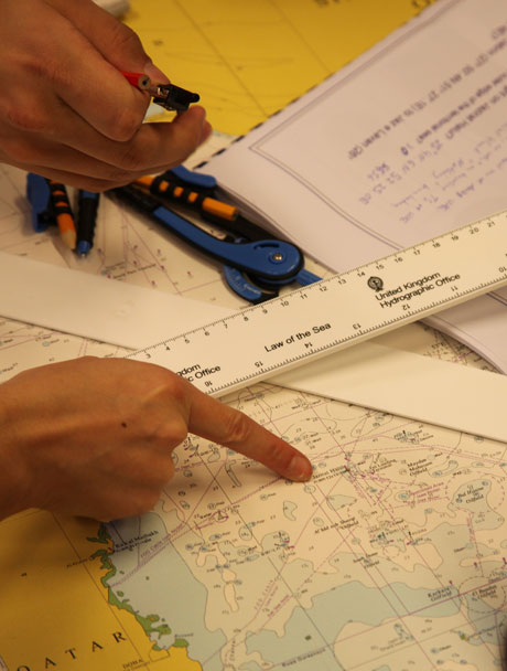 Studerande pekar på ett sjökort. Linjaler och passare.