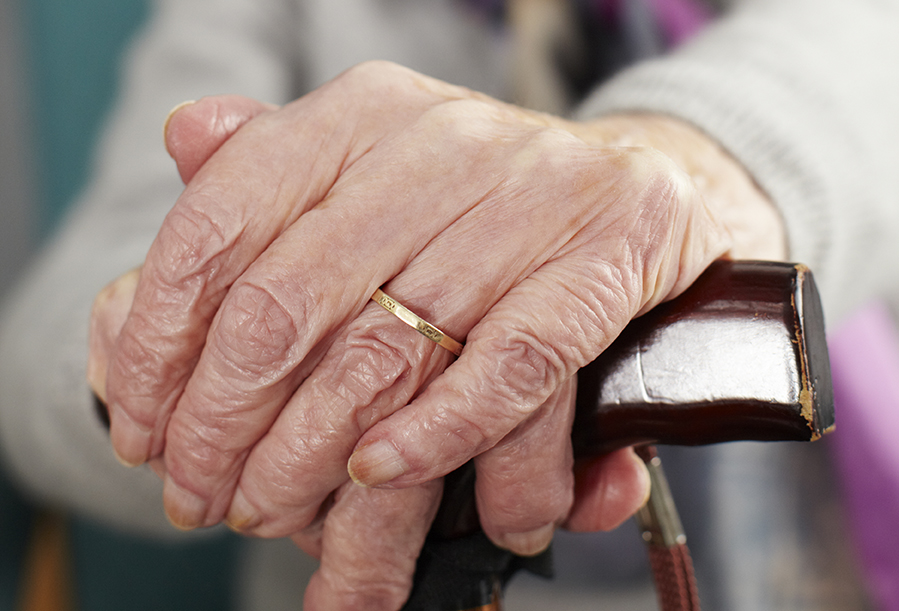 närbild på händer från en gammal person som håller en käpp
