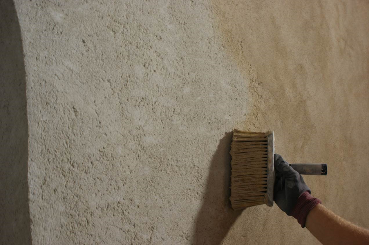 Stor vägg med en hand som håller i en borste och borstar puts