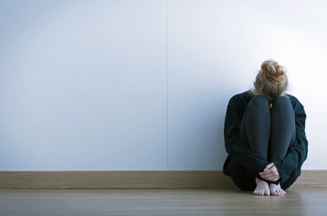 Genre picture of young woman in an empty room, sitting on the floor with her head down.