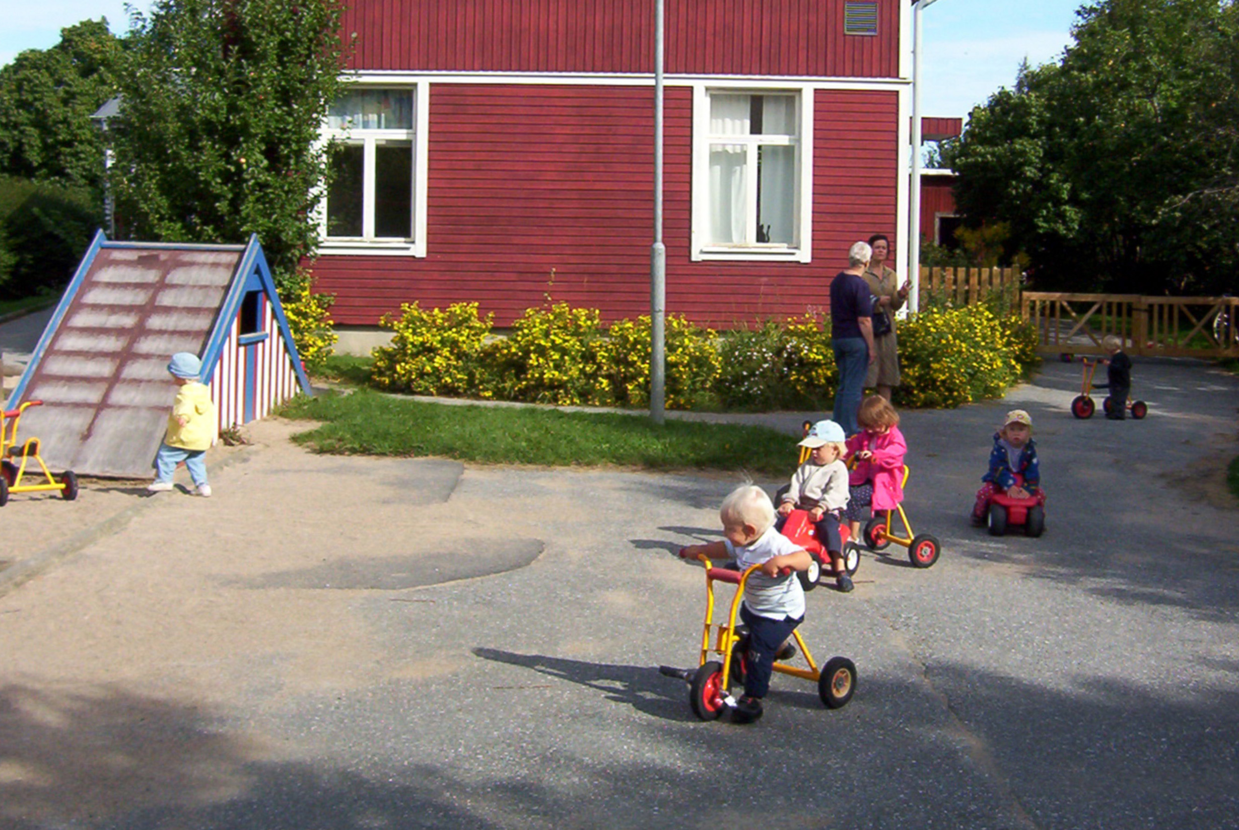 Förskolegård där barn leker och åker på små cyklar.