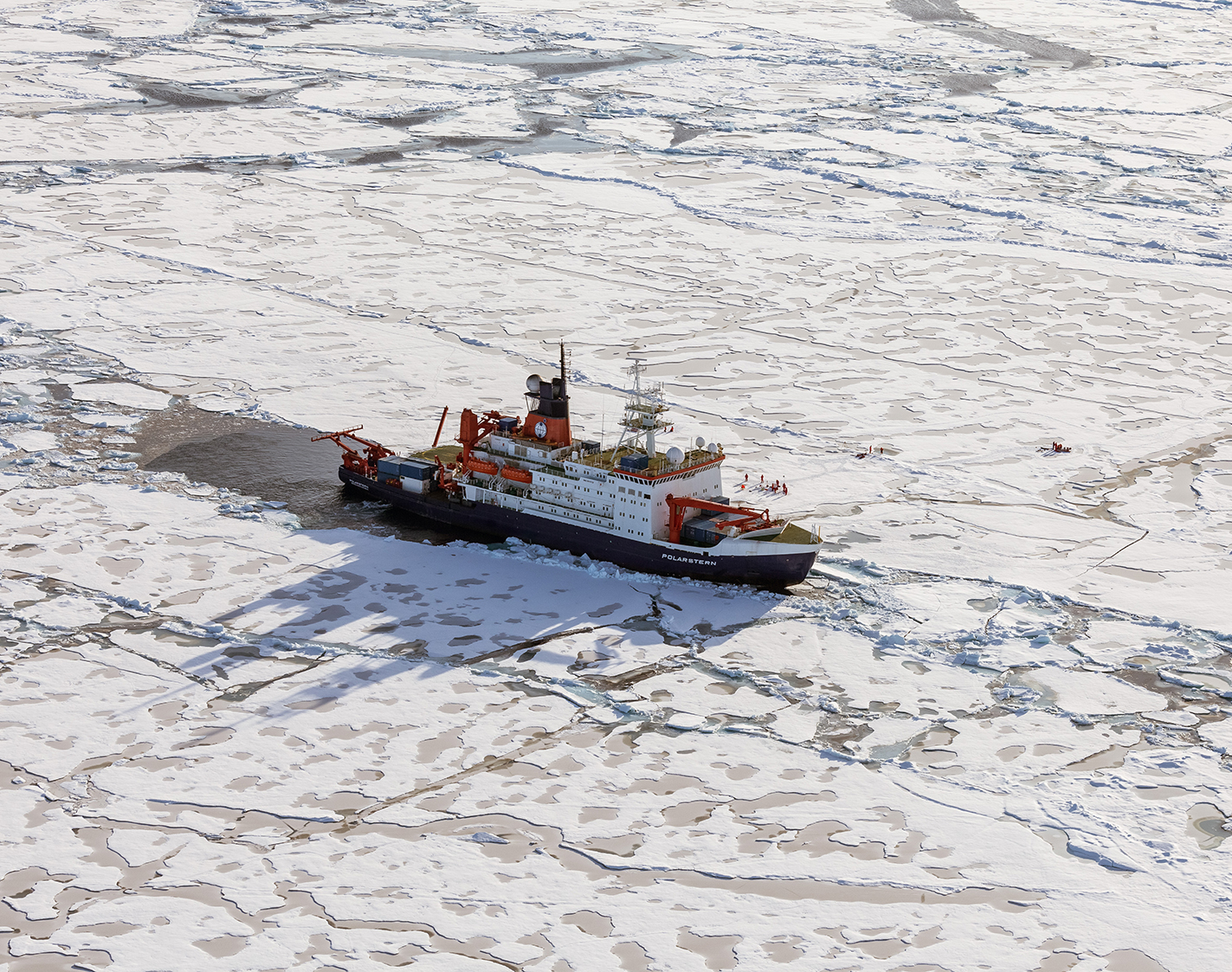 Fältarbetare på isen vid sin isbrytare. Sedda ovanifrån i dagsljus.