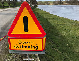 Varningsskylt för översvämning intill å.