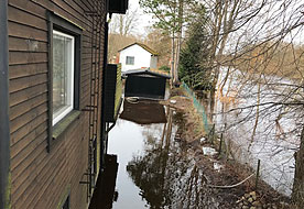 Hus med vatten runtom. Översvämmad å i bakgrunden.