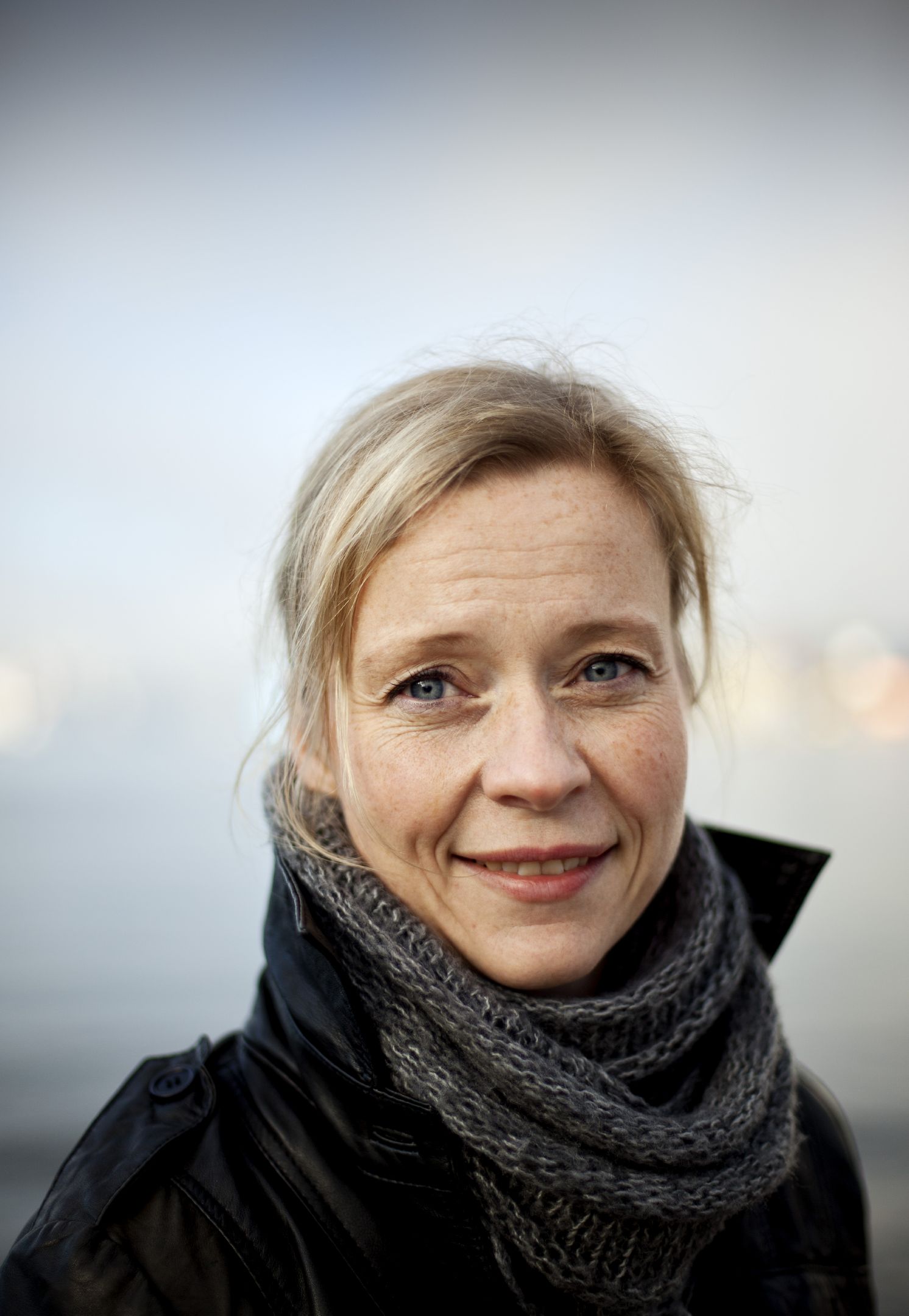 Porträttbild på Sofia Thorsson som tittar in i kameran. Hon har jacka och halsduk på sig och bakrunden är en skiftande himmel. 