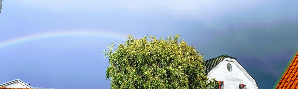 Sun is shining on rainy streets. Rainbow over the houses. 