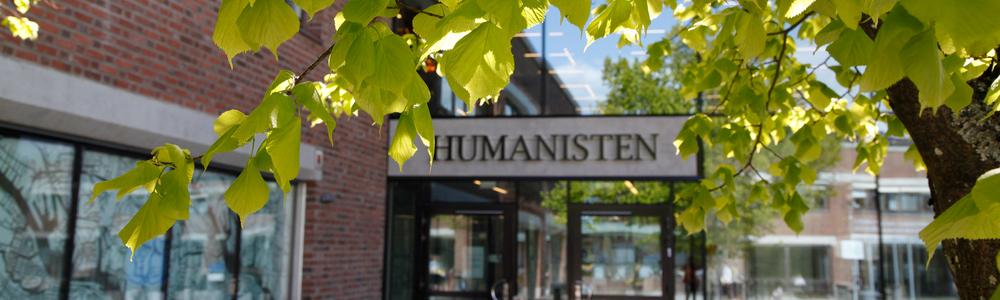 Entrén till Humanistiska fakultetens byggnad Humanisten i solsken. Blad i förgrunden. 