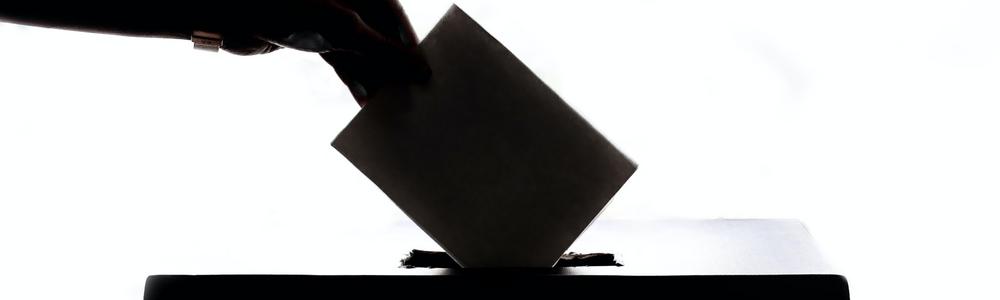 En hand lägger ner en röstsedel i en låda.