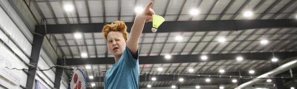 Pojke i gymnastikhall på väg att slå serve i badminton