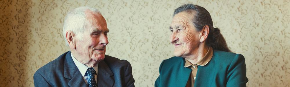 An elderly couple looks at each other and smiles.
