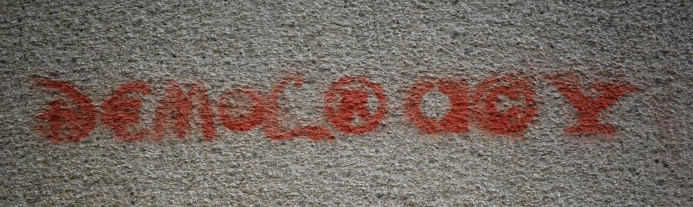 the word democracy written in red on a stone wall