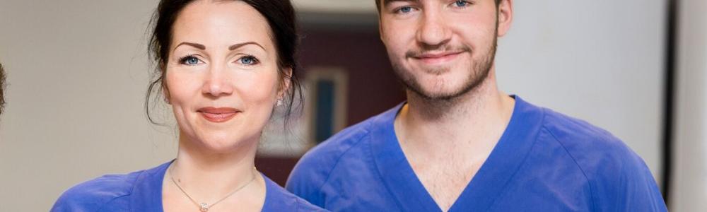 en tjej och en kille med vårdkläder tittar rakt in i kameran 