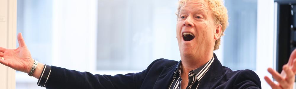 Bo Rosenkull sjungandes och med utsträckta armar i en undervisningssituation bakom en flygel