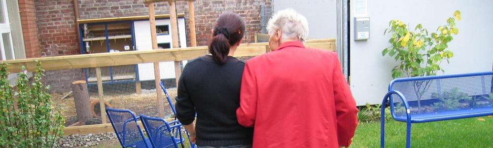 en person stödjer en äldre människa på en promenad utomhus 