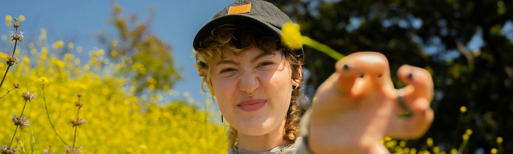 en person står vid en äng och håller upp en blomma