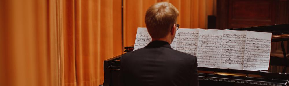 Pianist sitter vid flygel med stort notblad