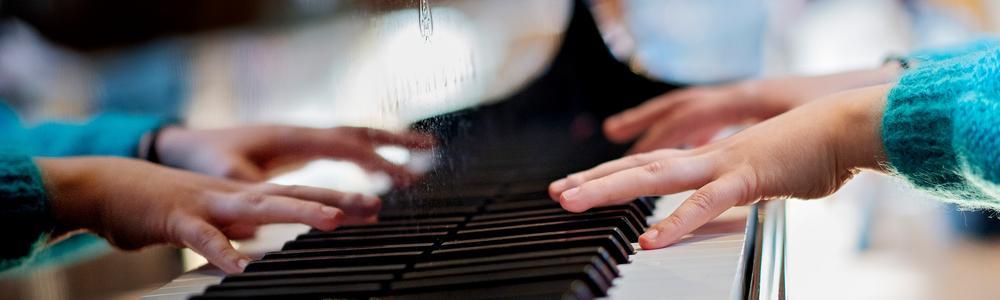 Händer på tangenterna på en flygel. Spegelbilden syns i flygeln.