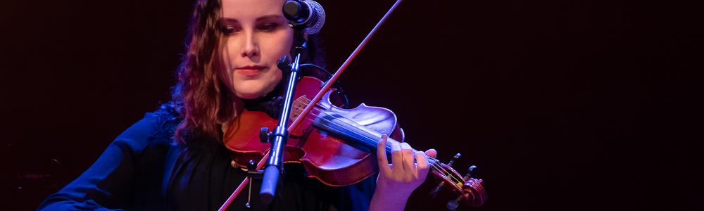 En student spelar fiol i ett mörkt rum