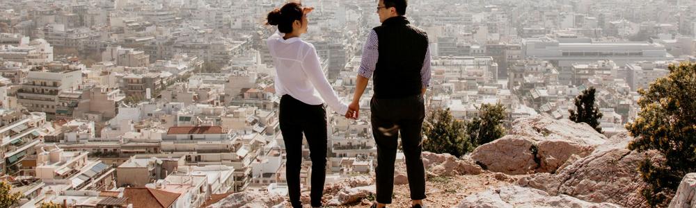 Två personer håller varandra i handen och tittar ut över en stad.