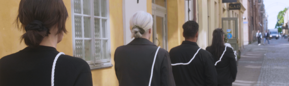 Four people walk in a line along a street in an urban setting.