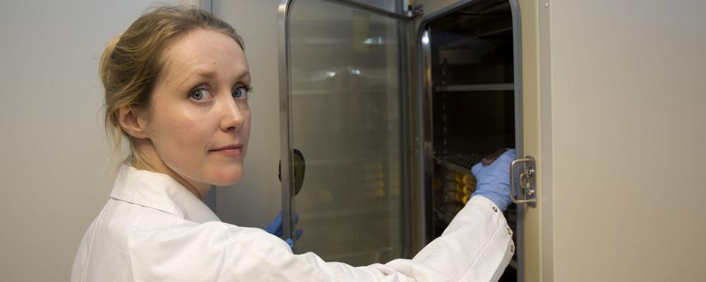 Forskaren Emma Börgeson klädd i vit labbrock öppnar dörren till ett skåp med provrör.