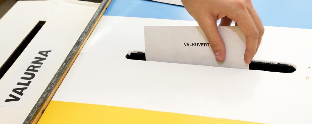 Hand som lägger röstkort i rösturna på valdagen
