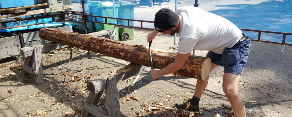 Bilden visar en man som barkar en timmerstock