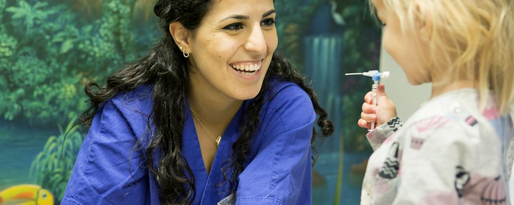 en barnsjuksköterska ler mot ett barn i en vårdmiljö