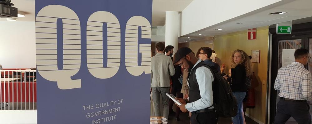 People standing next to a poster with the Quality of Government logo while reading from information brochures