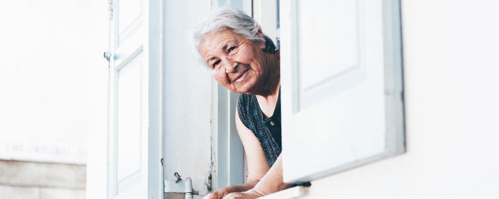 Äldre kvinna tittar ut genom ett öppet fönster