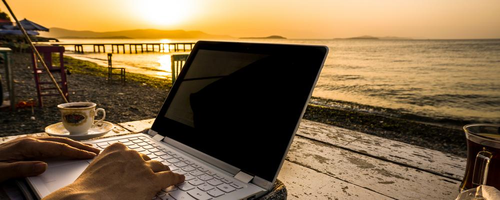 Författare arbetar framför datorn på en strand vid havet