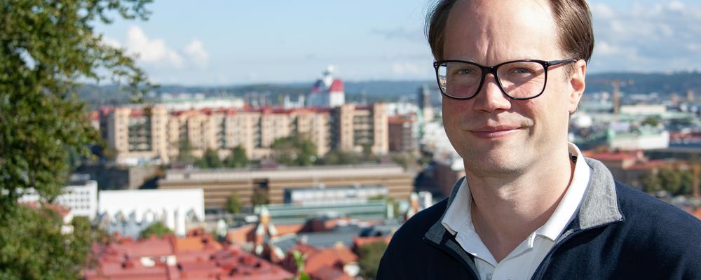 En man står med utsikt över Göteborg bakom sig. Av centrala staden syns bostadshus med röda hustak, en orange lyftkran, parkområden och kontorsbyggnader som till exempel den röd-vita skyskrapan vid Lilla Bommen som många kallar för Läppstiftet.