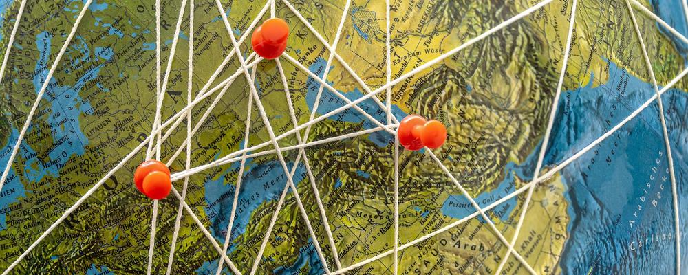 Jordglob med kartnålar och trådar som binder samman olika delar av världen, fotografi. 
