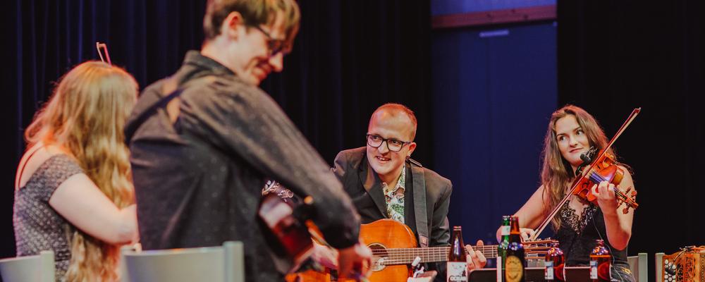 En grupp musiker sitter runt ett bord på scen och spelar tillsammans.