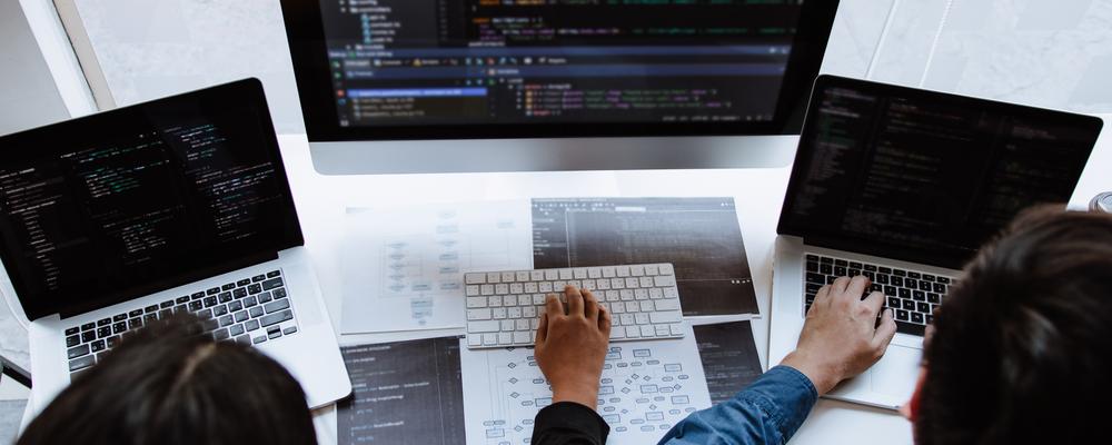 Foto på två personer framför flera datorskärmar