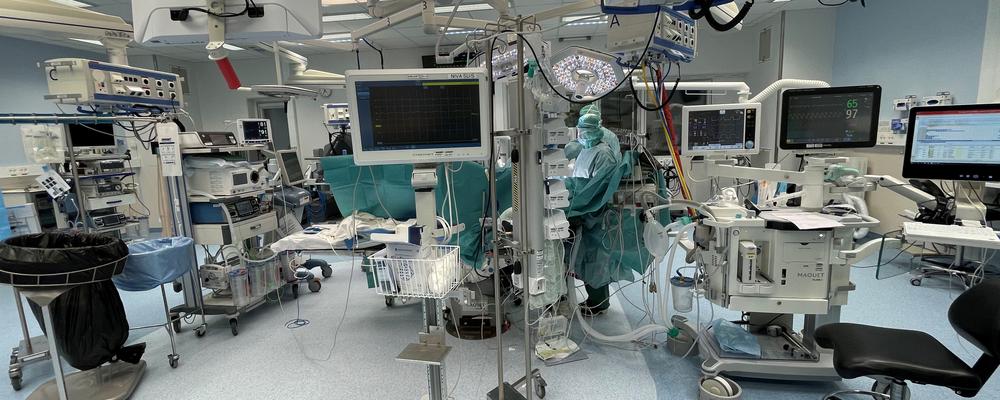 Överblicksbild över operationsrum, med en mängd monitorer. Operation pågår i bakre delen av rummet.