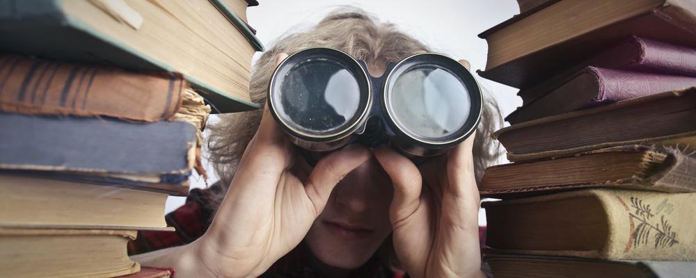 Woman using binoculars to serch for something in books