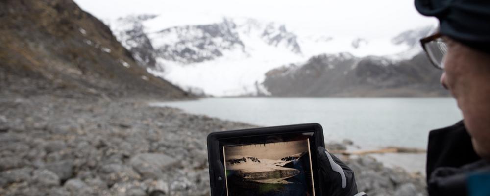 A person is holding an image in a arctic landscape.