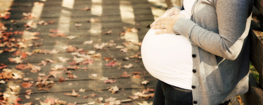 Ensam gravid kvinna har stannat till utomhus, med händeran på magen, hon ser ut att fundera