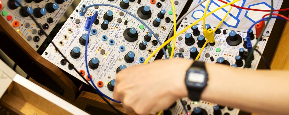 A hand tweeking a knob on a synthesizer