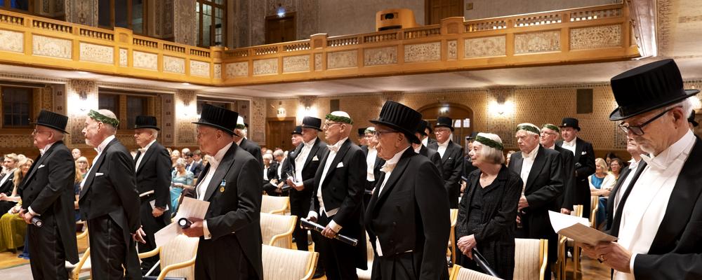 Högtidlig bild från kreeringen av jubeldoktorer 2021 - frackar och klänningar och höga hattar i den pampiga salen i universitetets huvudbyggnad i Vasaparken.